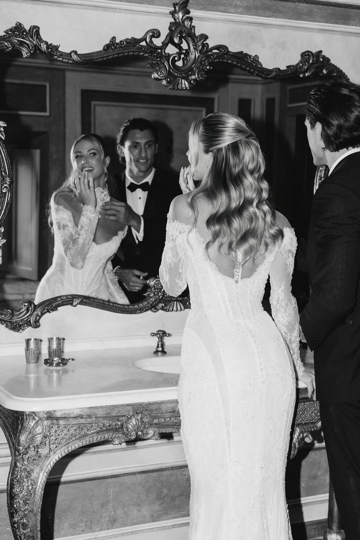 The bride at a marble washstand, she and the groom reflected in a carved gilt mirror