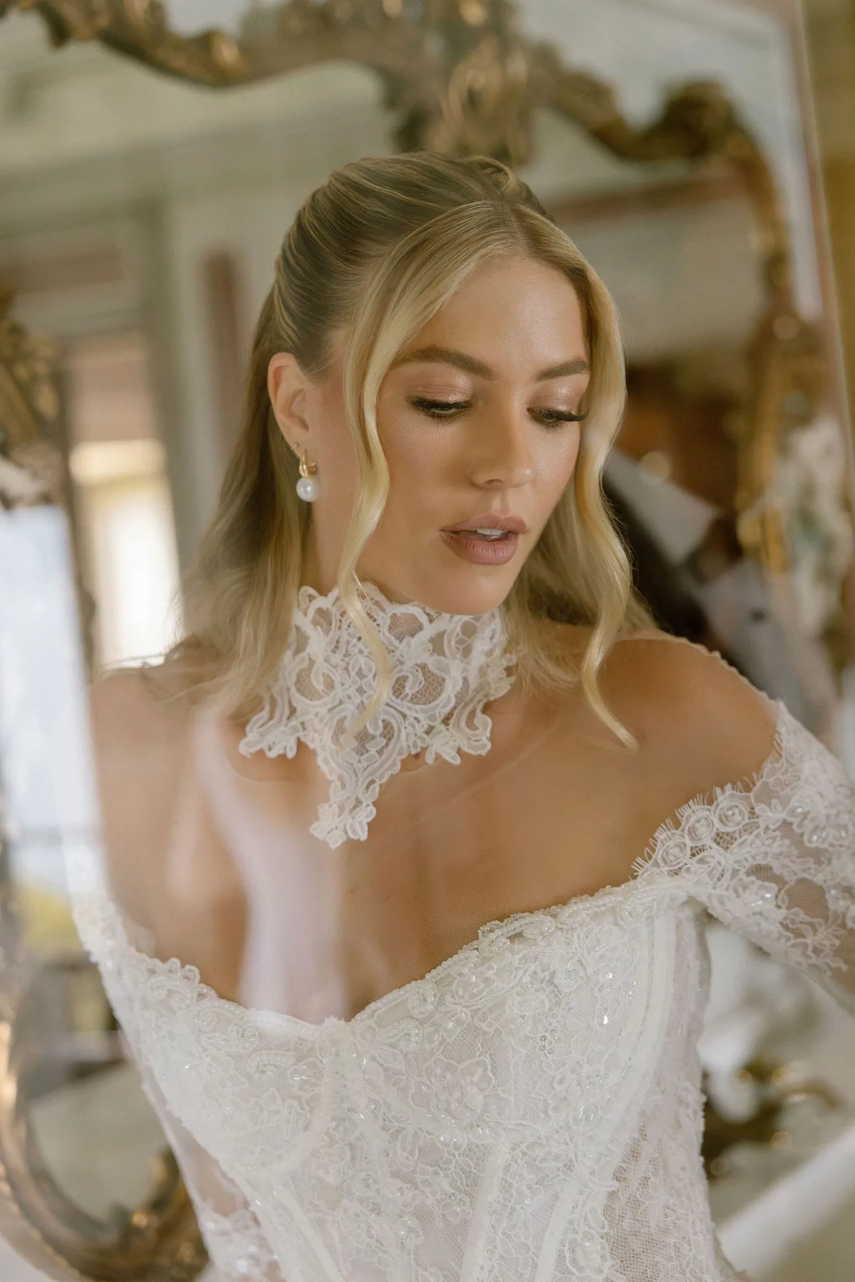 The bride in an off-shoulder lace gown with a high lace collar, a gilt mirror behind her