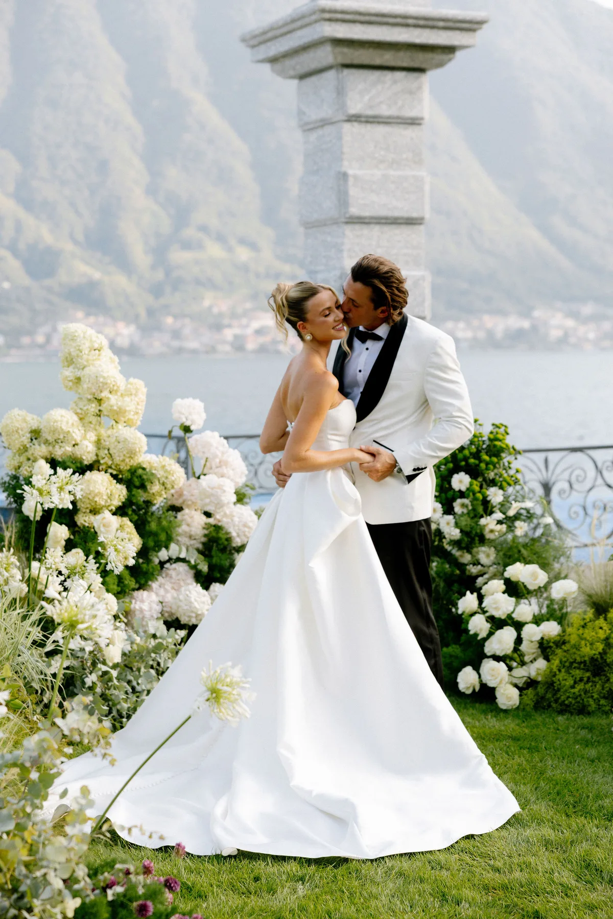 The couple among white hydrangeas on the lawn, the lake and mountains behind
