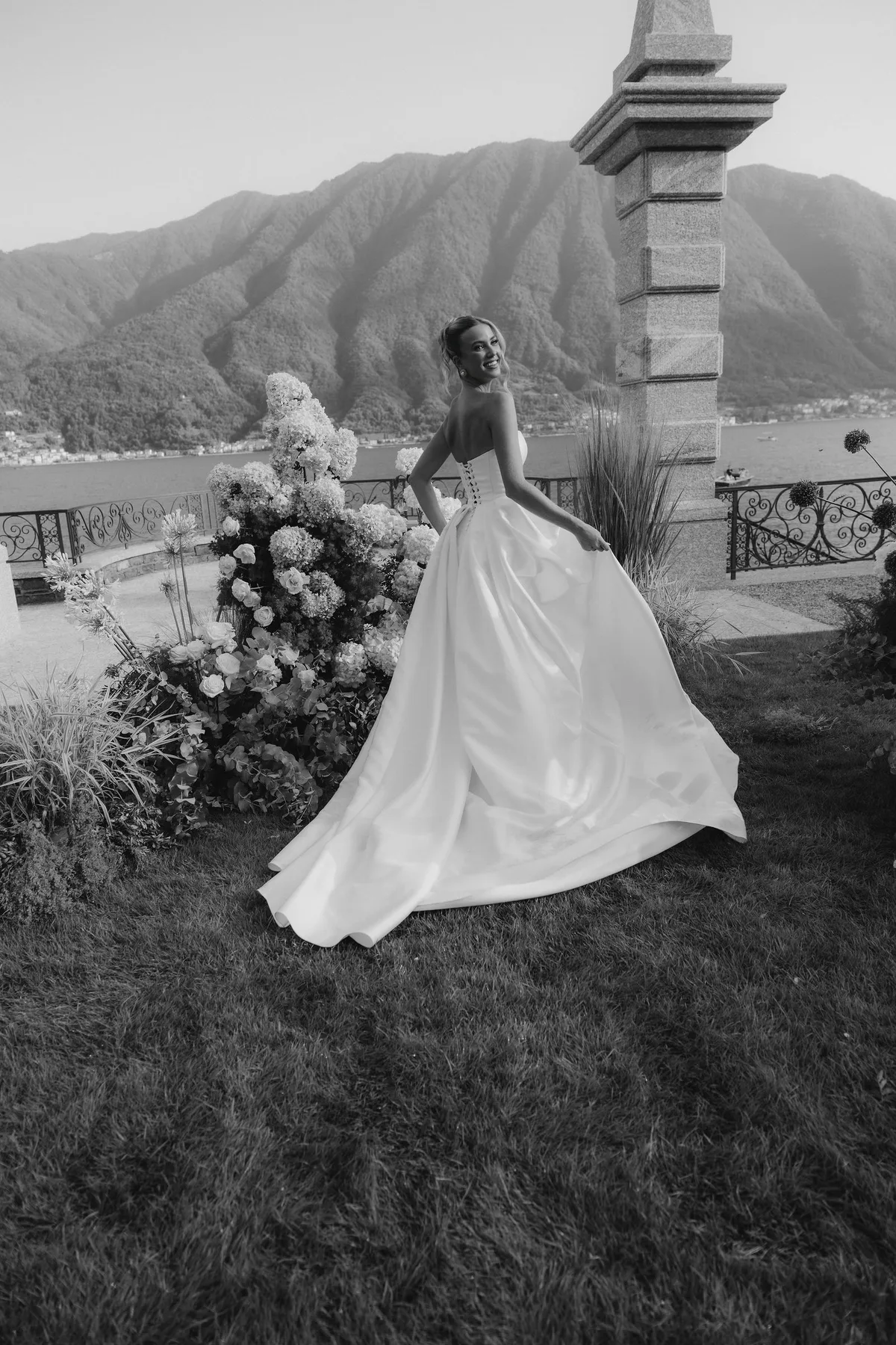 The bride turning on the grass, her skirt sweeping, flowers and the lake behind