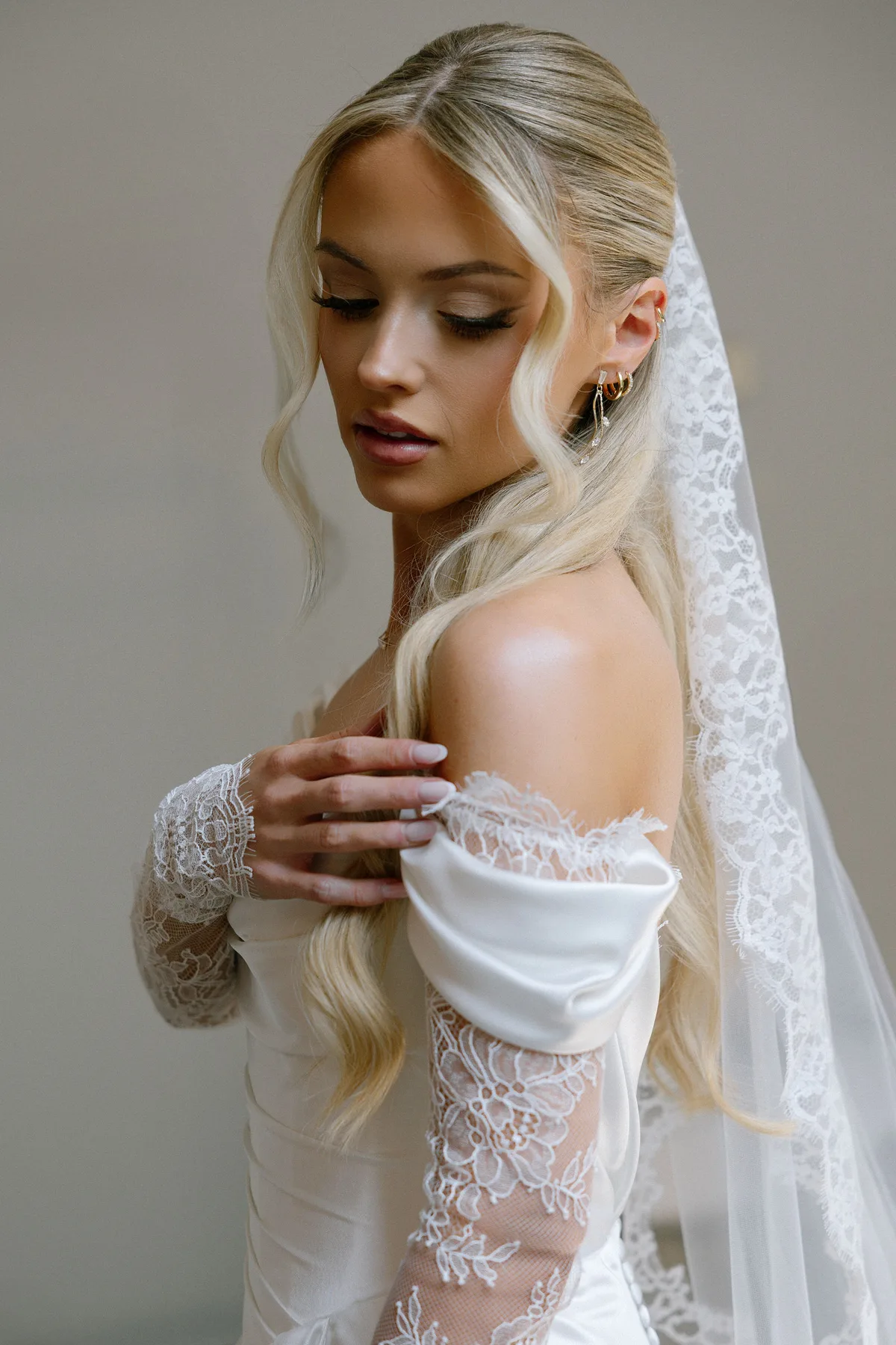 The bride in a satin gown with lace sleeves, her veil over one shoulder