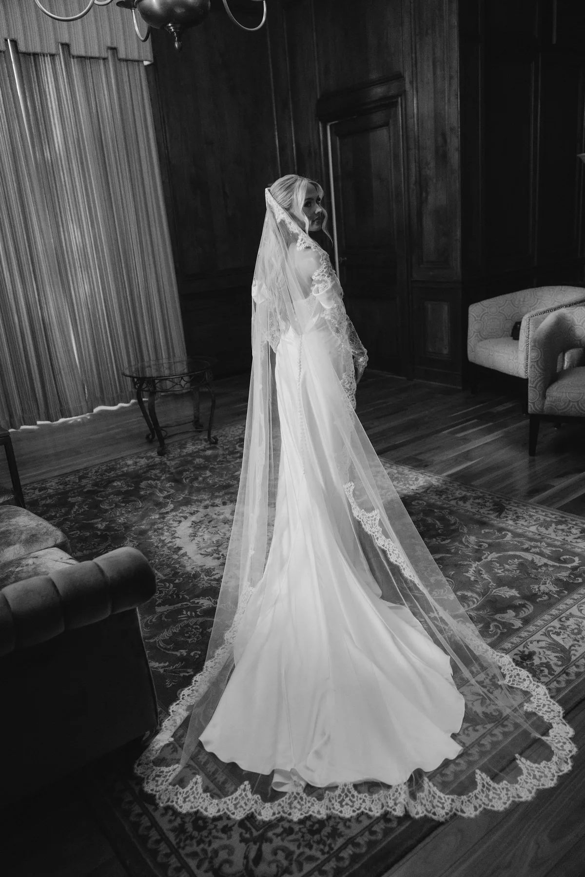 The bride alone in a panelled room, her lace-edged veil spread across the rug