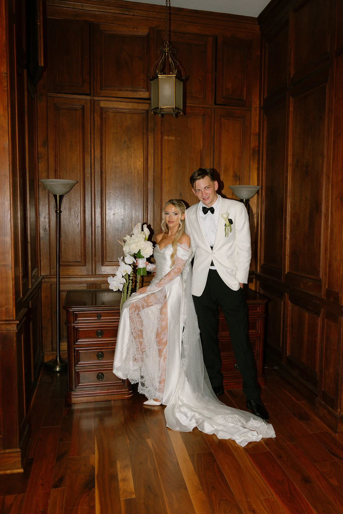 The couple in a wood-panelled room, the bride holding white orchids
