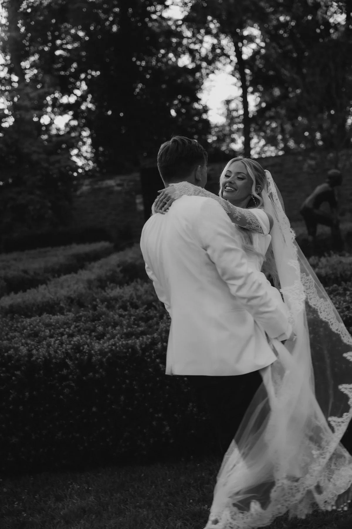 The groom lifting the bride on the lawn, her veil sweeping behind