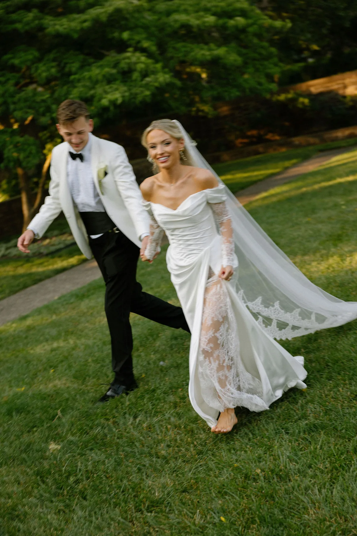 Bride and groom walking barefoot across the grass, her train trailing