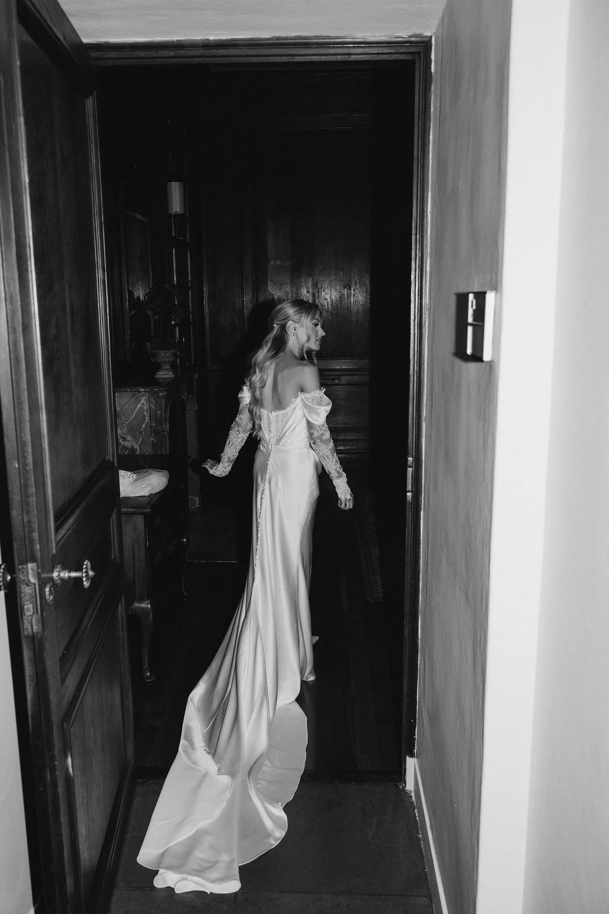 The bride walking away down a dark panelled corridor, her train behind her