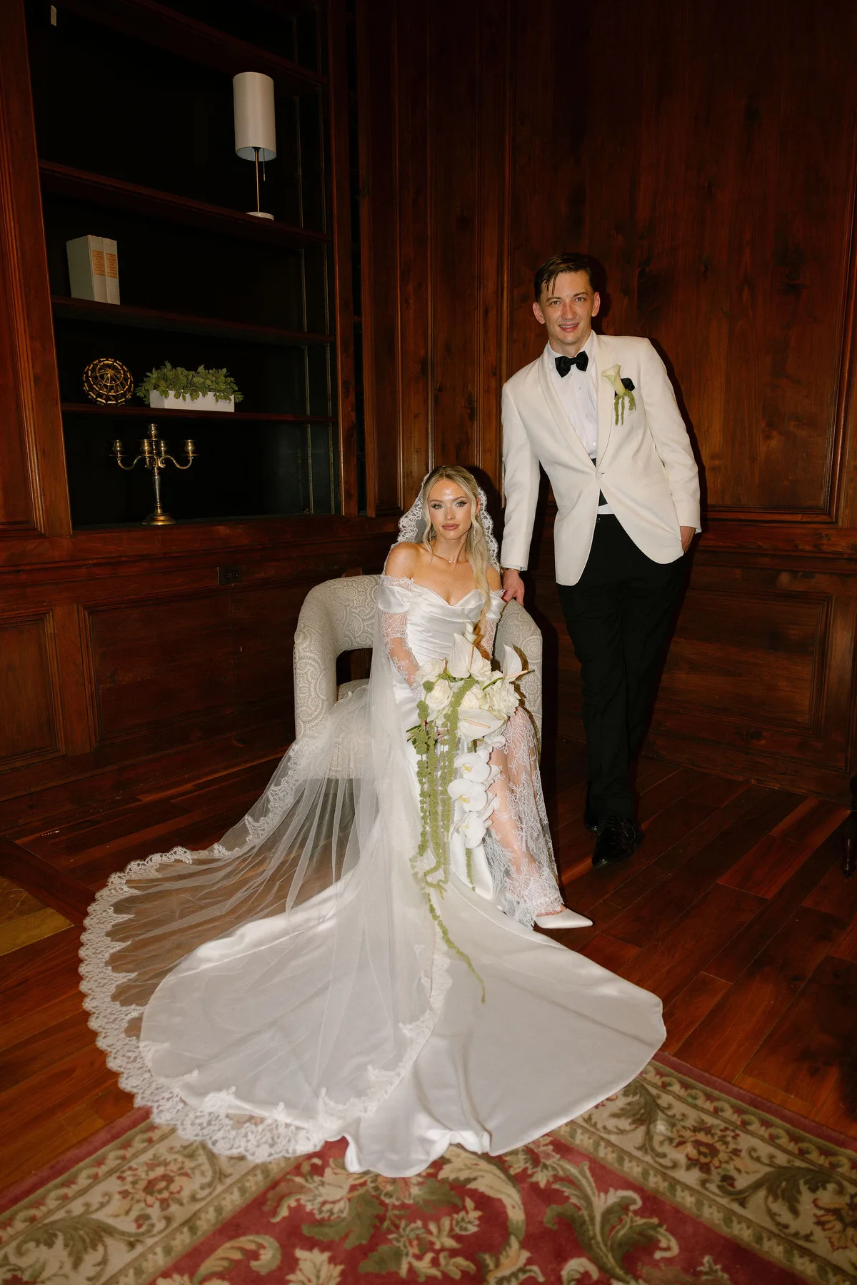 The couple in a panelled room, the bride seated with her train spread on the rug