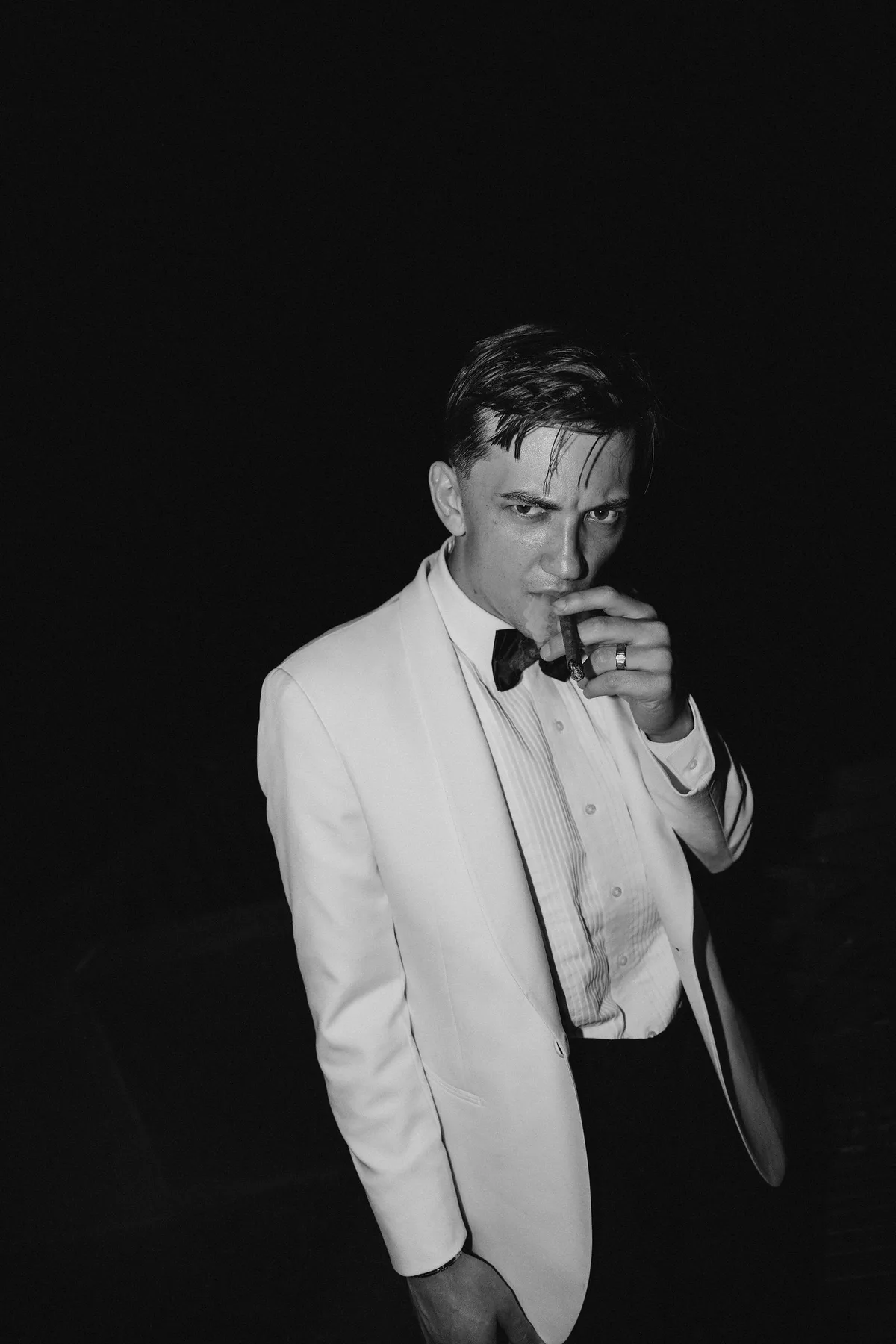 The groom in a white dinner jacket against black, hand raised to his chin