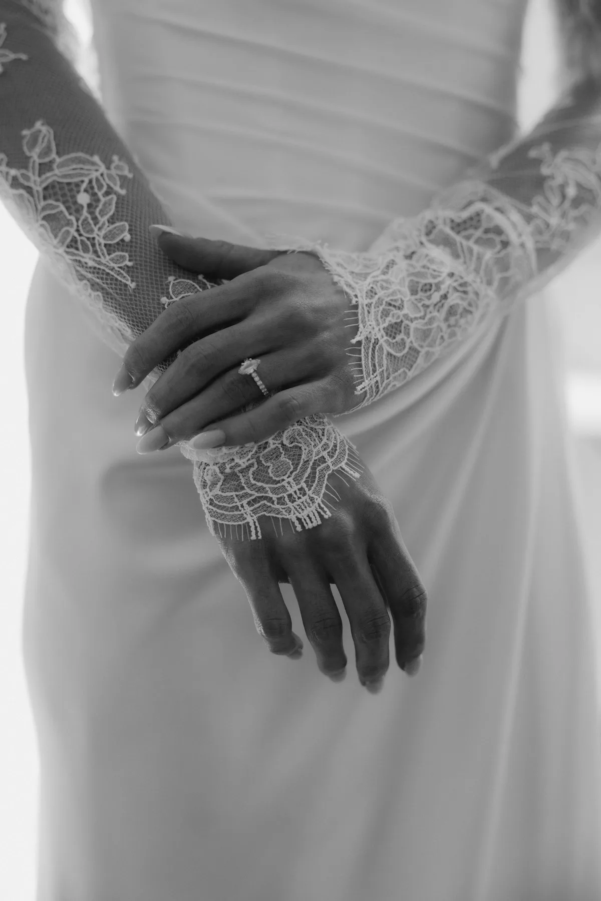 The bride's hands crossed at her waist, her rings and lace cuffs