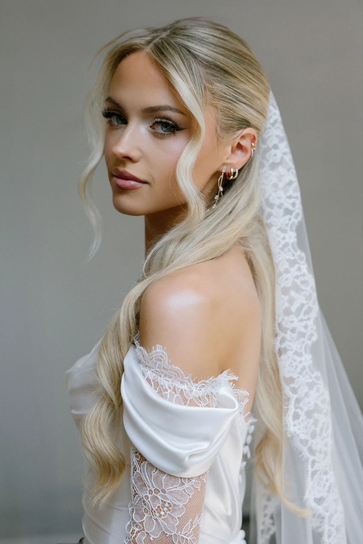The bride in profile, her veil over her shoulder, against a plain wall