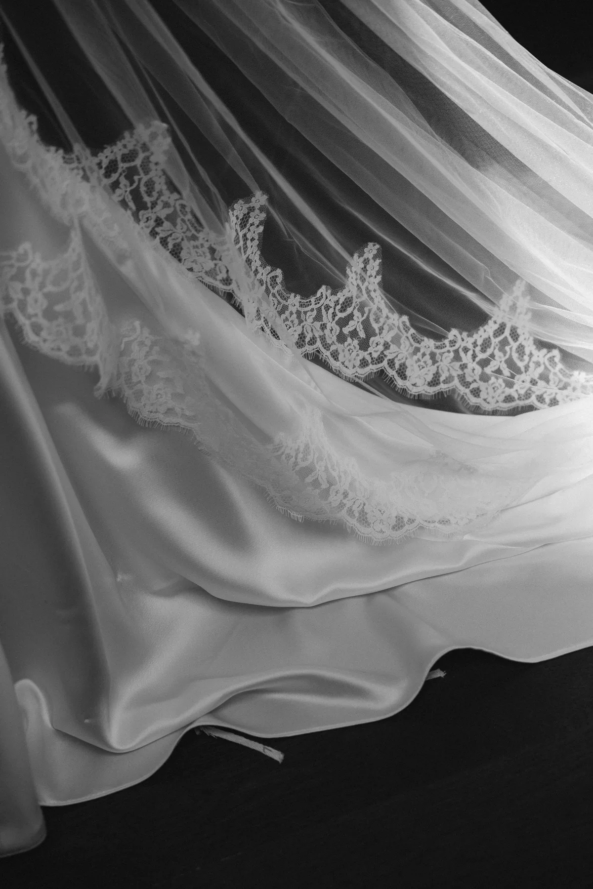 The lace hem of the bride's veil across the fall of her satin skirt