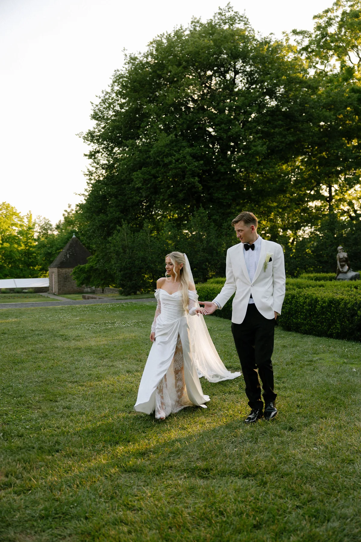 The couple walking across the lawn hand in hand, parkland behind them