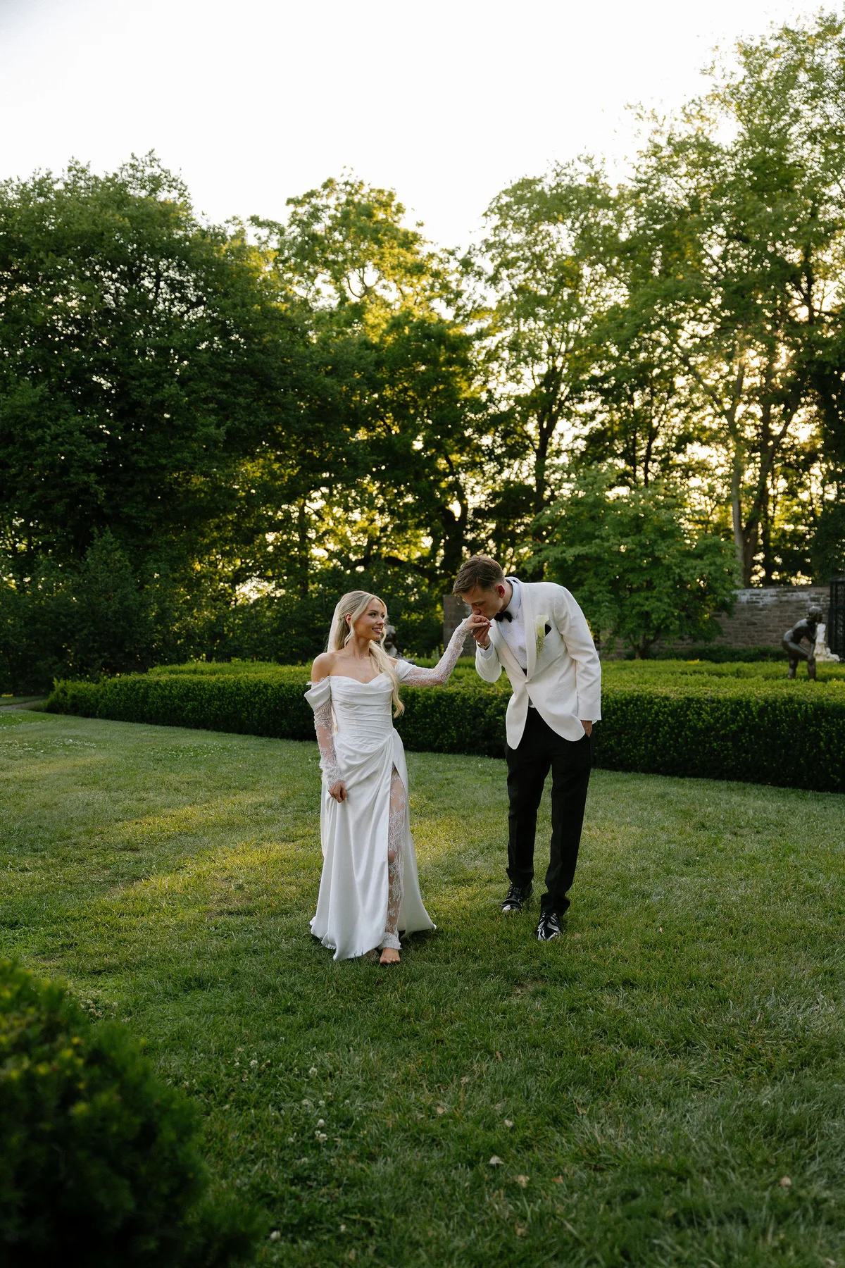 The groom bowing to kiss the bride's hand on the lawn