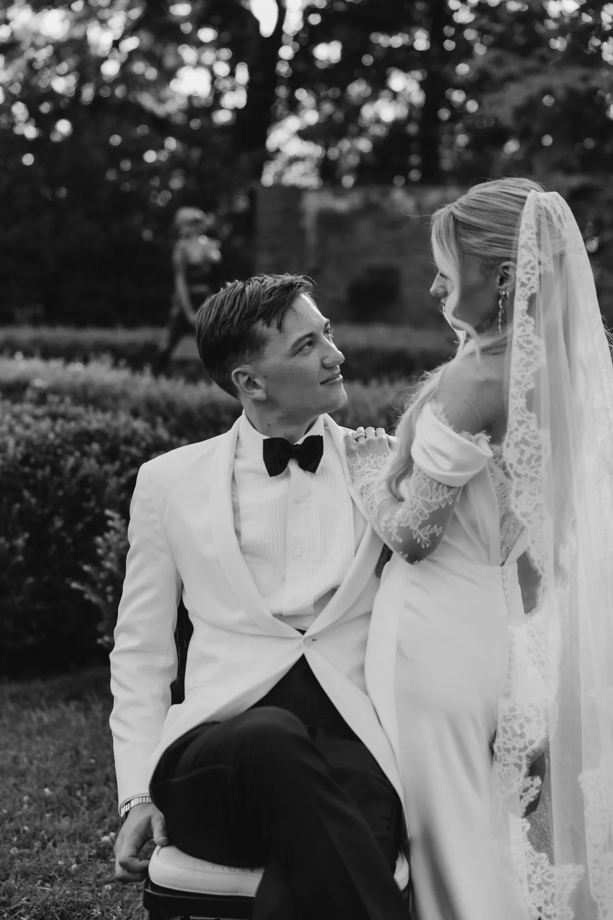 The bride standing over the seated groom in the garden, both laughing
