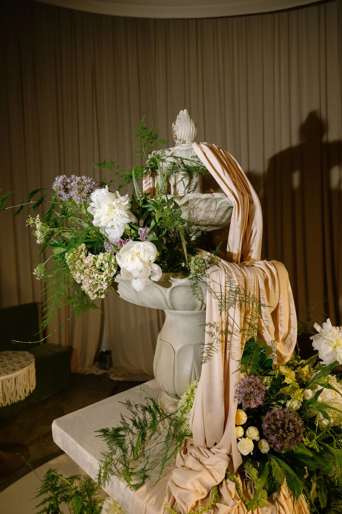 A stone fountain dressed with peonies and draped silk at the reception