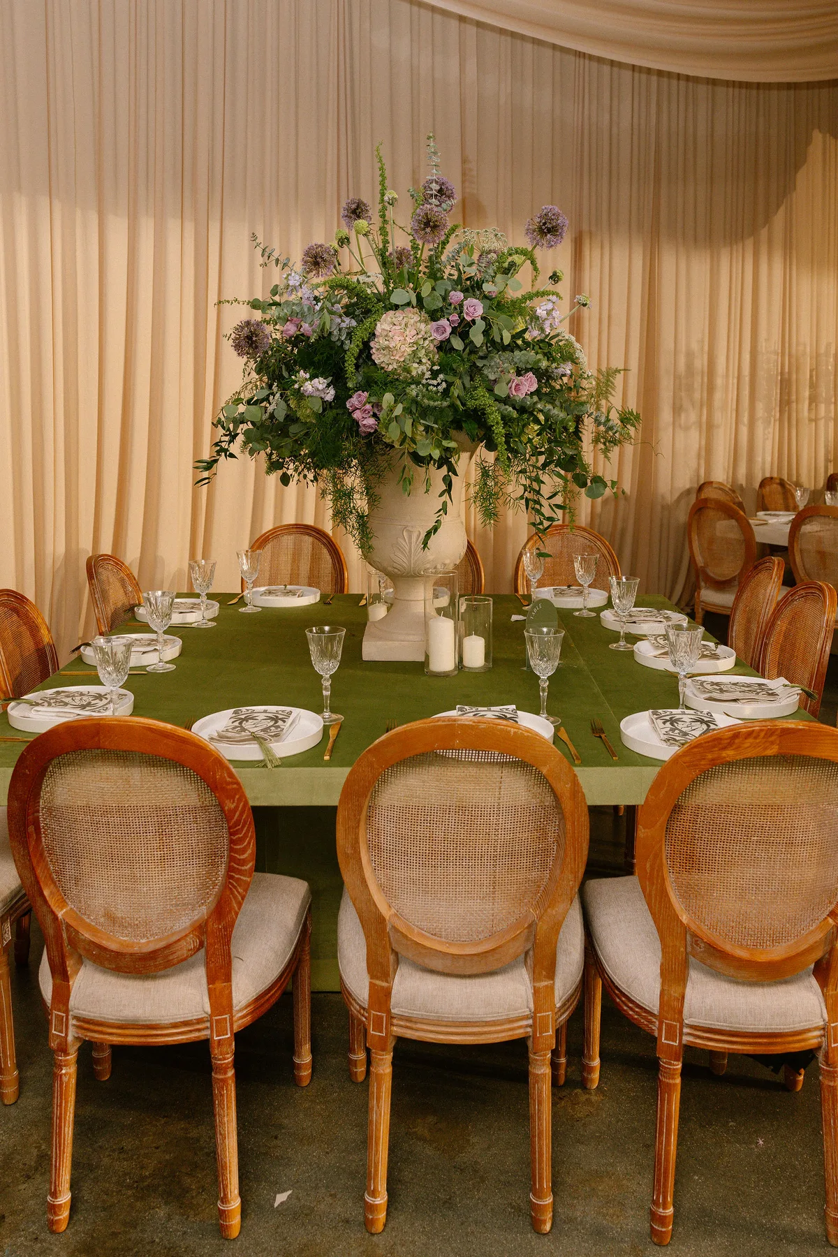 A round table laid on green cloth, cane chairs and a tall urn of flowers
