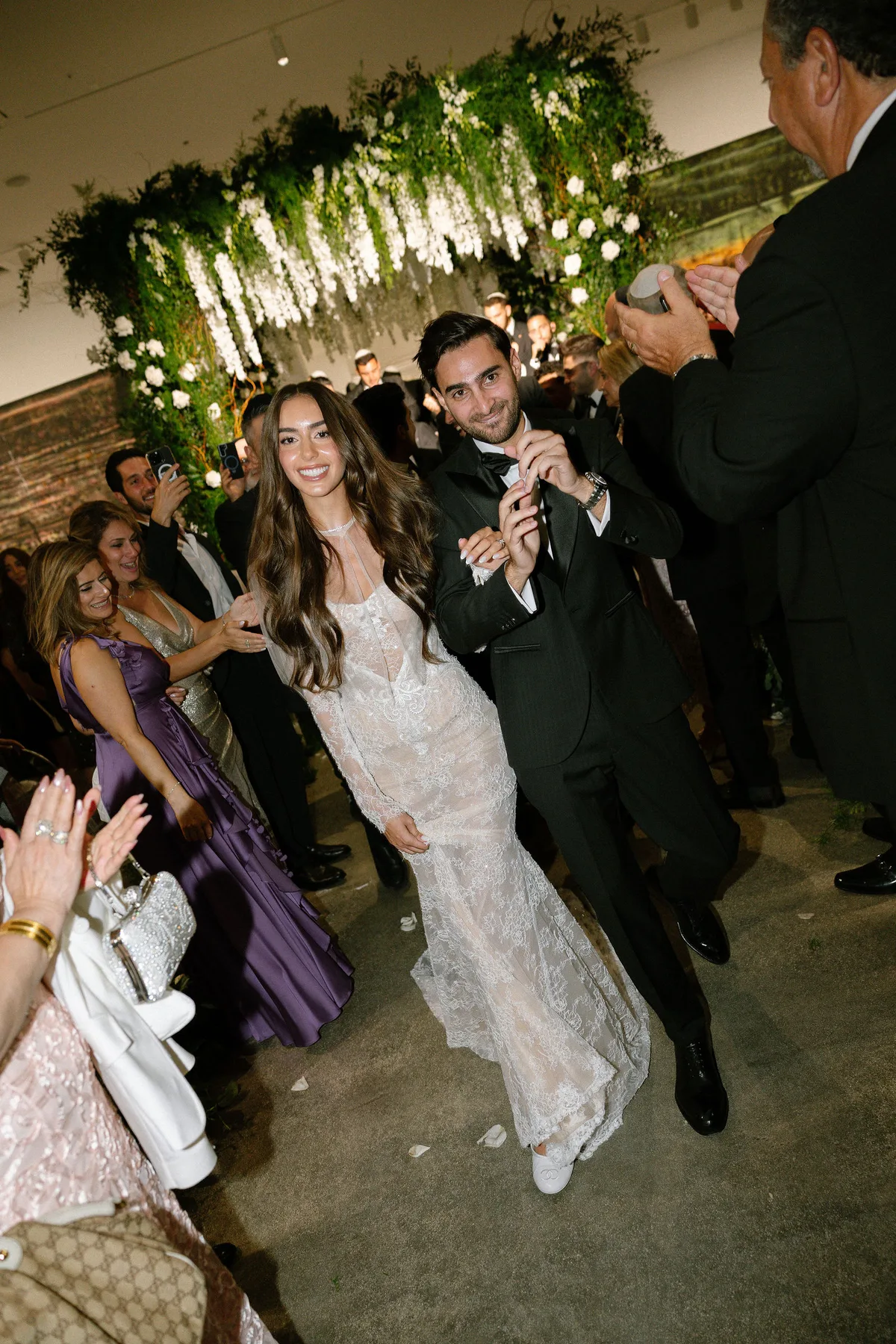 Bride and groom coming back up the aisle under a hanging flower canopy, guests applauding