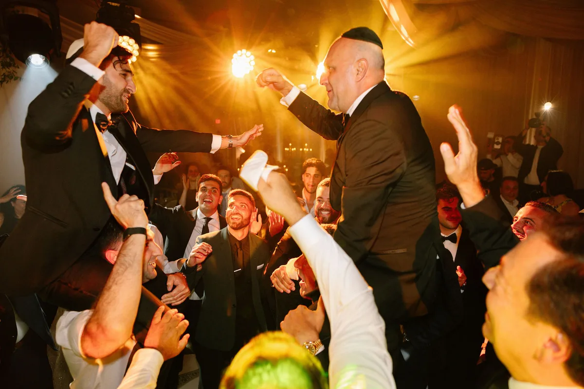 The groom lifted on a chair by the men of the party, the room in warm light