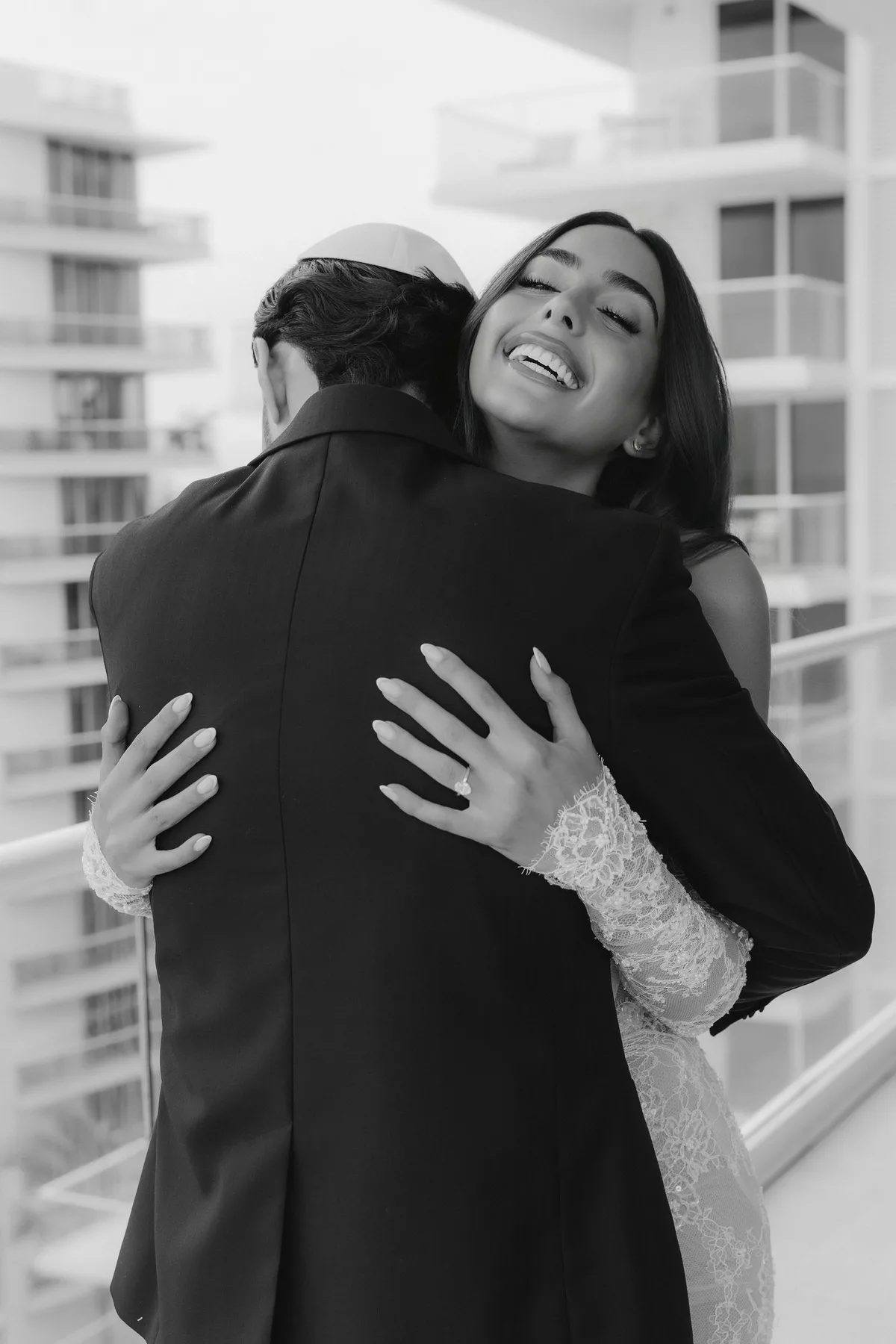 The bride laughing with her arms around the groom on a balcony