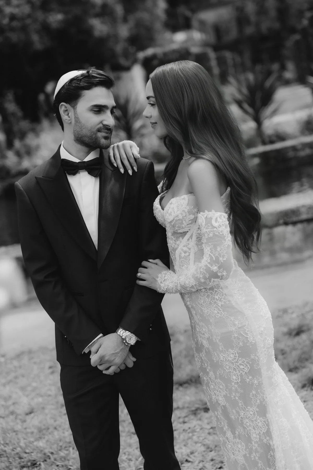 The couple close together on a garden path, his hands holding hers