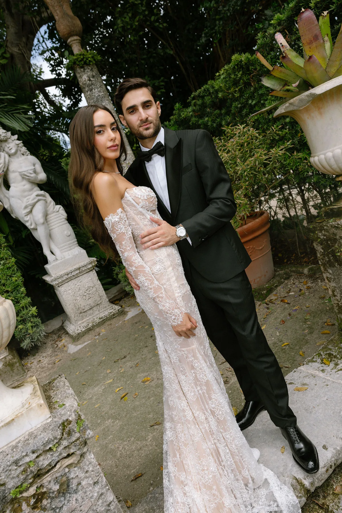 Bride and groom among statues and planting in a walled garden