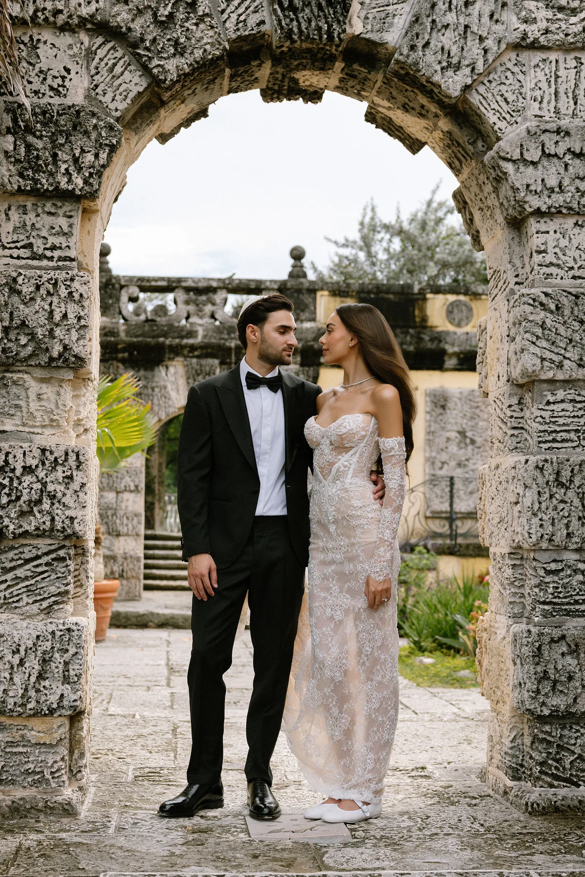 The couple framed by a coral-stone arch, the garden beyond