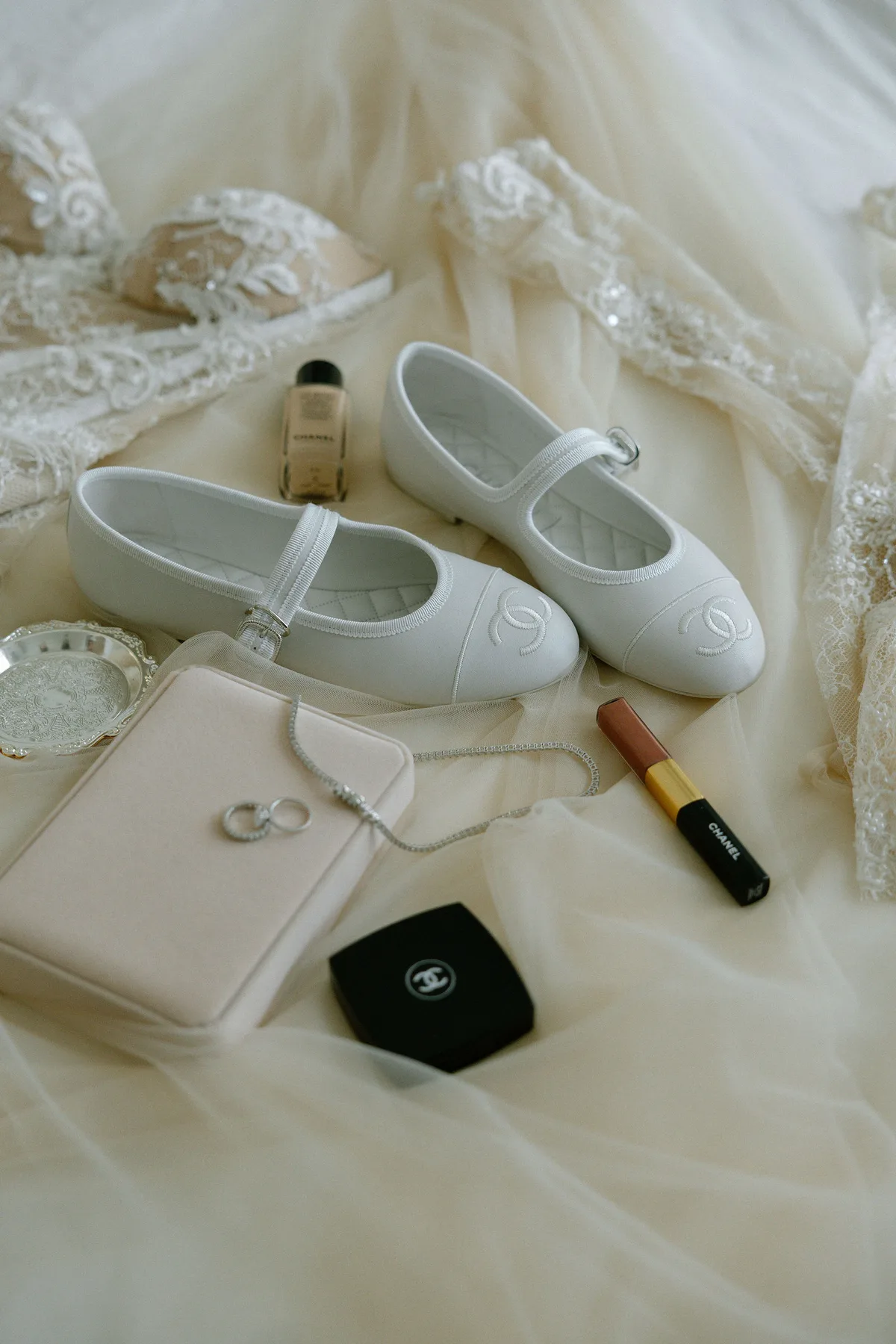 The bride's flat shoes, rings, perfume and lipstick laid out on her veil