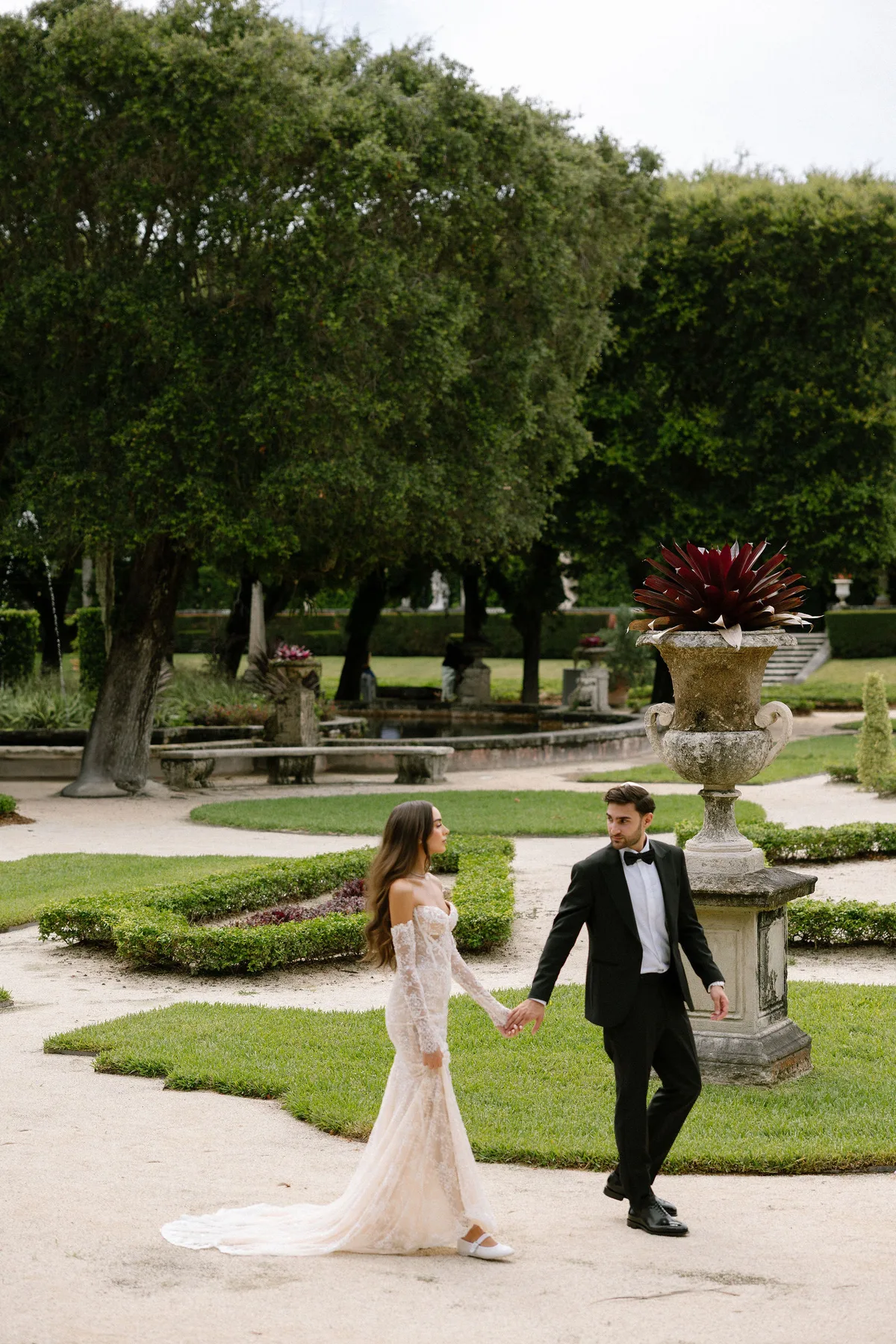 Bride and groom walking hand in hand through a parterre garden