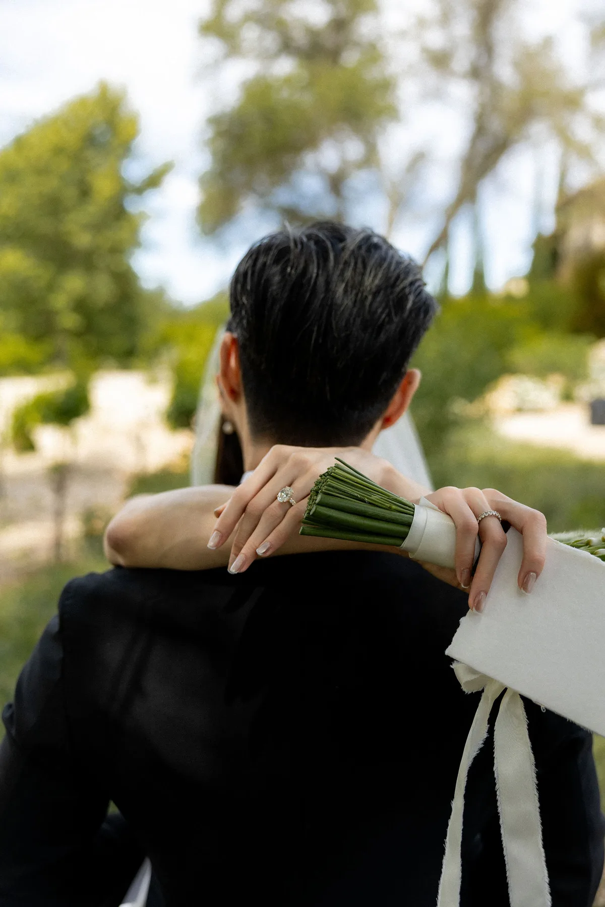 The bride's hands on the groom's shoulder from behind, bouquet in one hand
