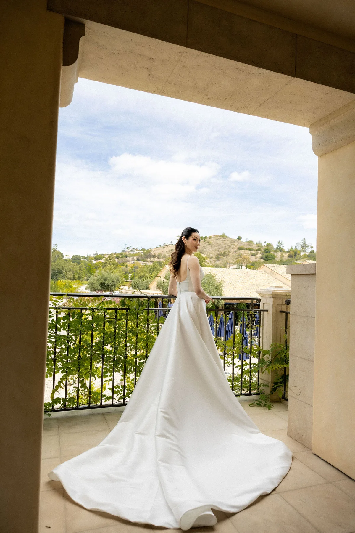 The bride on a stone loggia, her train spread across the floor, hills beyond