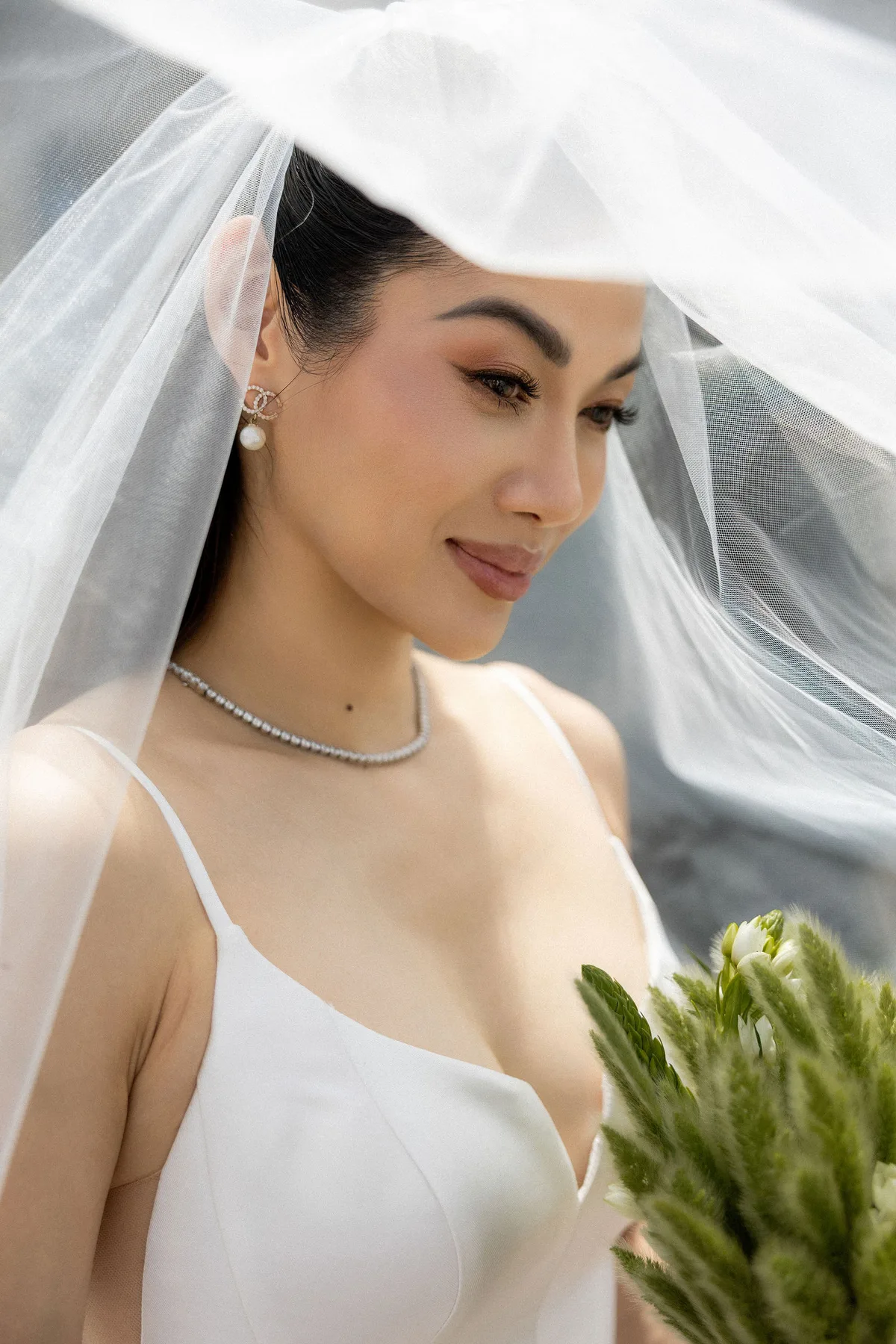The bride under a lifted veil, her necklace and bouquet in the frame