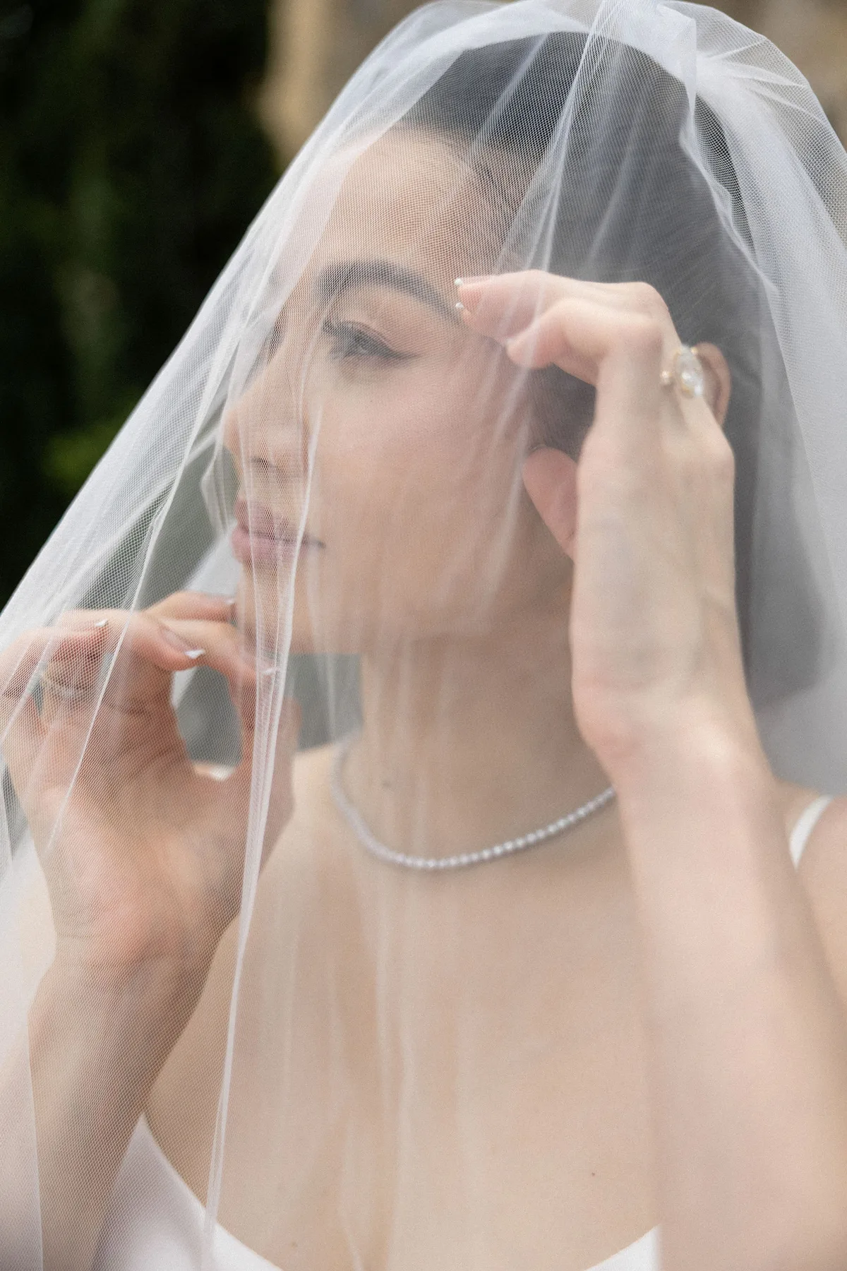 The bride raising her veil with both hands, her face behind the tulle