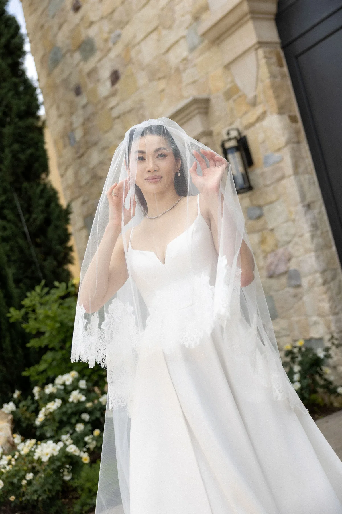 The bride under her lace-edged veil against the stone wall of the winery