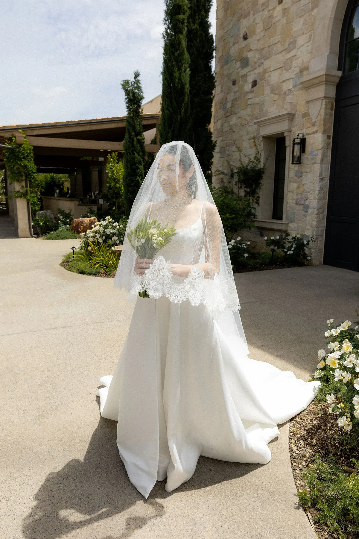 The bride walking up the drive with her bouquet, veil down