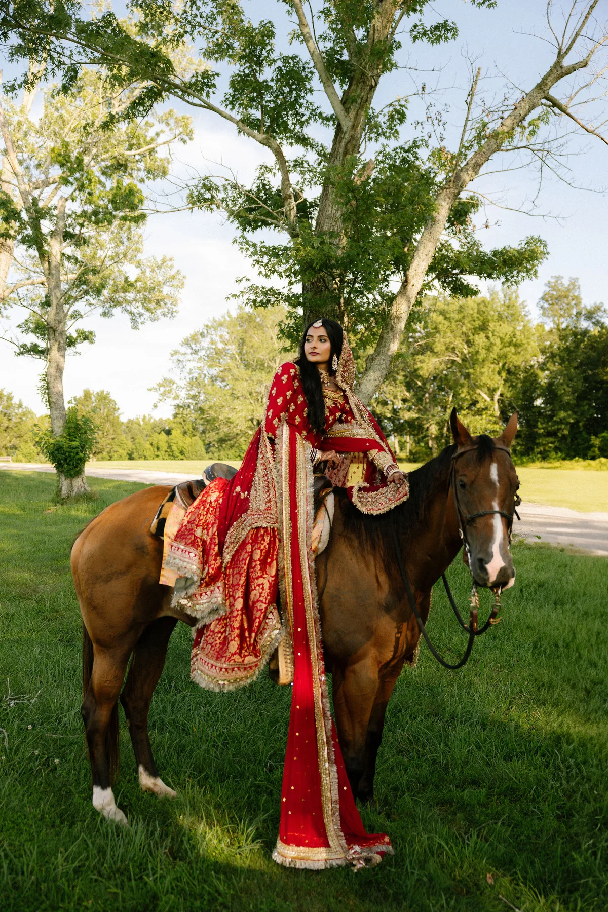 The bride mounted side-saddle in red and gold, under a spreading tree