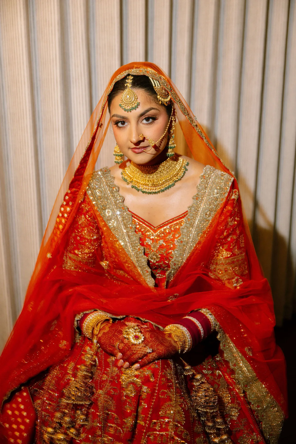The bride seated in full red and gold bridal dress and jewellery