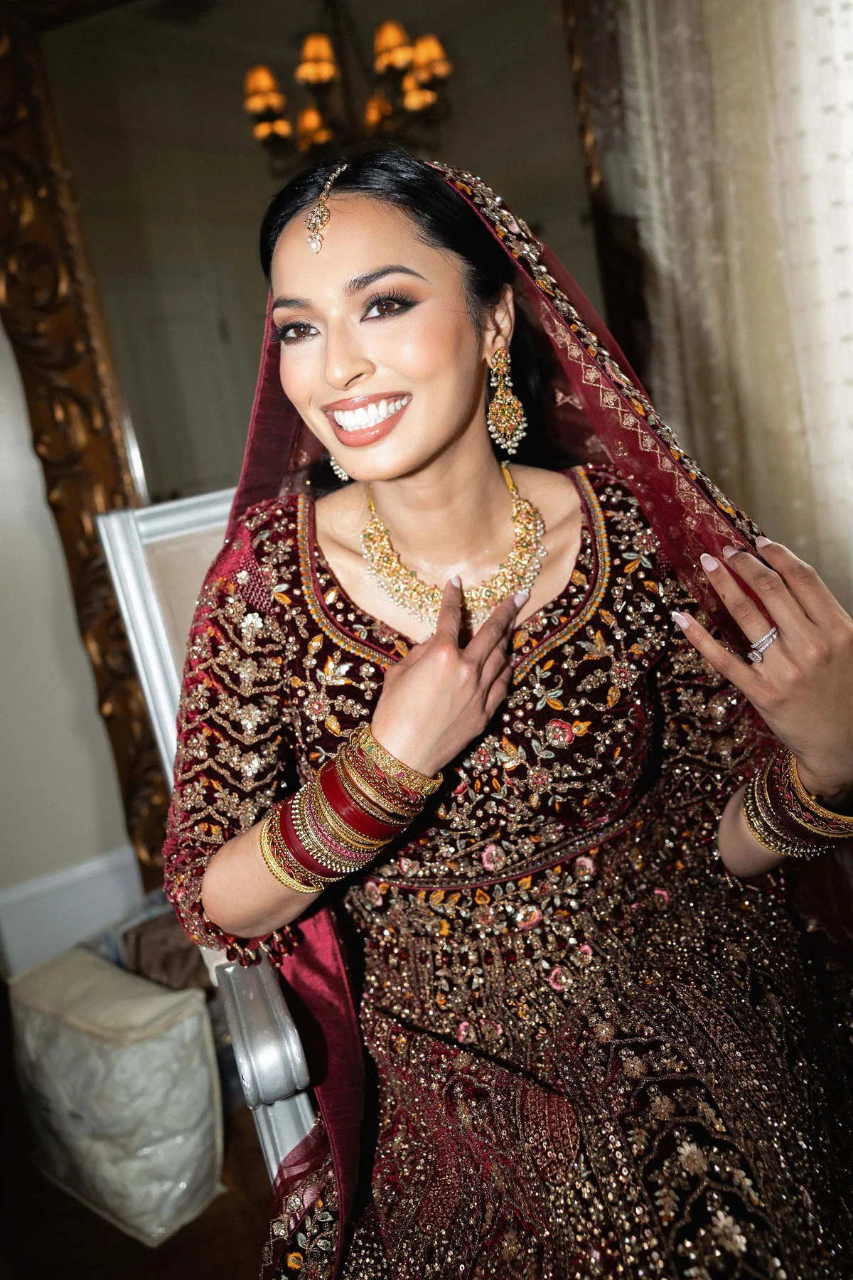 The bride laughing before a gilt mirror, hand to her necklace
