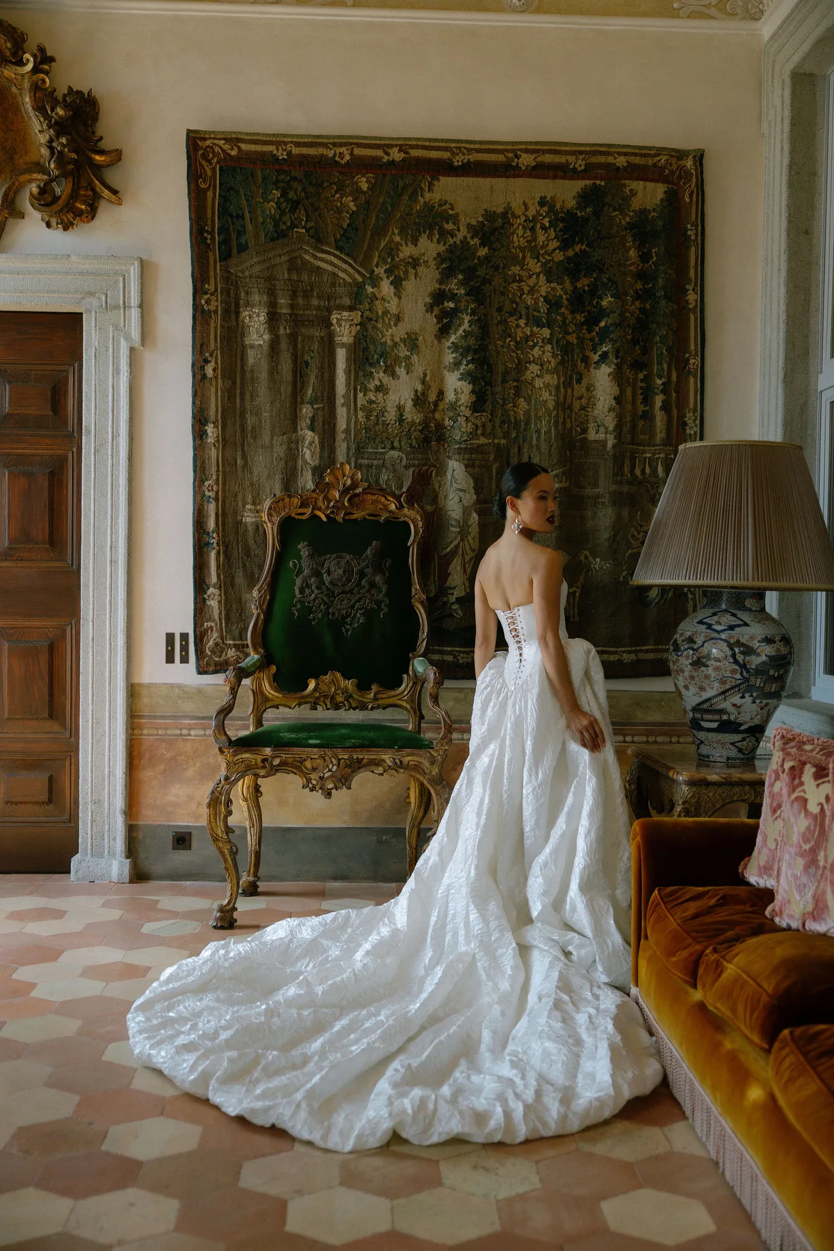 The bride from behind in a frescoed salon, her crumpled silk train across the tiles