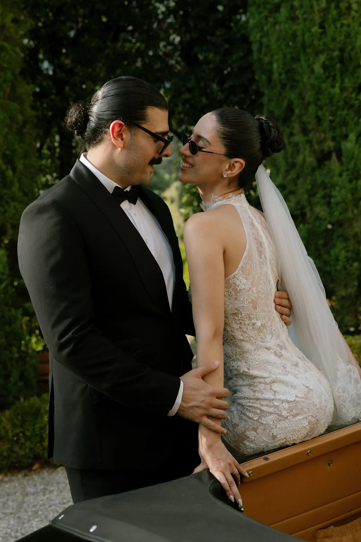 The couple in sunglasses, close, an open-topped car in front of them