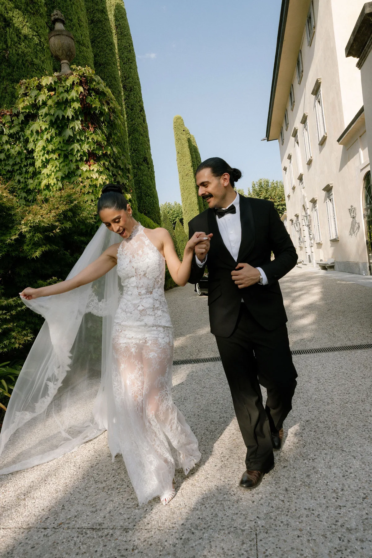 The couple running hand in hand along the villa wall, her veil streaming