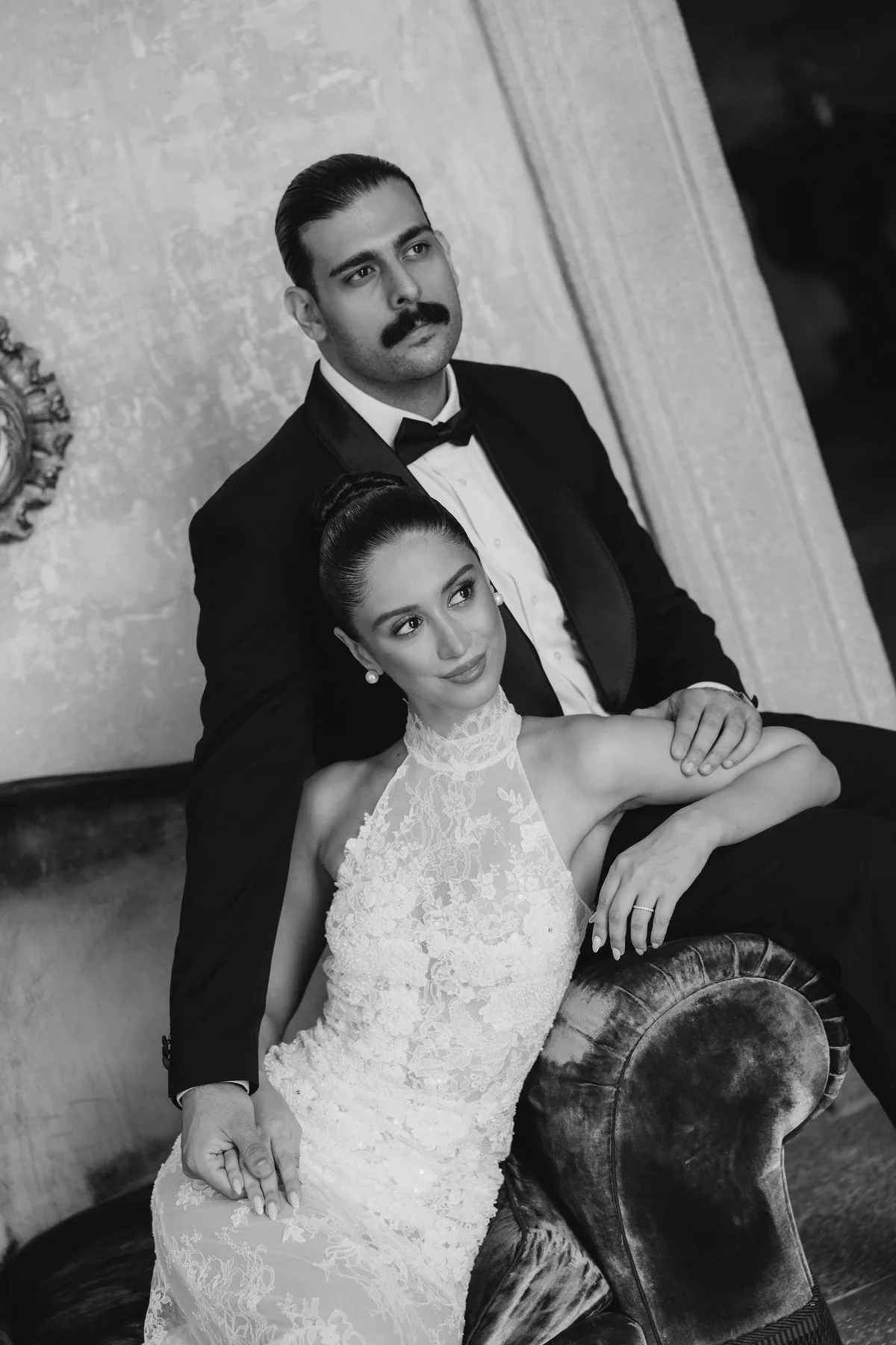 The couple on a velvet sofa, her arm along the back, the groom behind